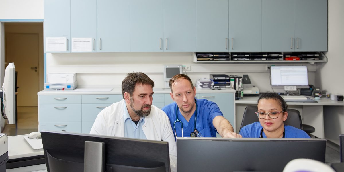 Drei medizinische Fachkräfte in einem Büro analysieren Daten auf Computerbildschirmen.