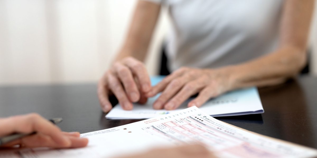 Two people sitting at a table reviewing forms. One person holds a pen, the other papers. 