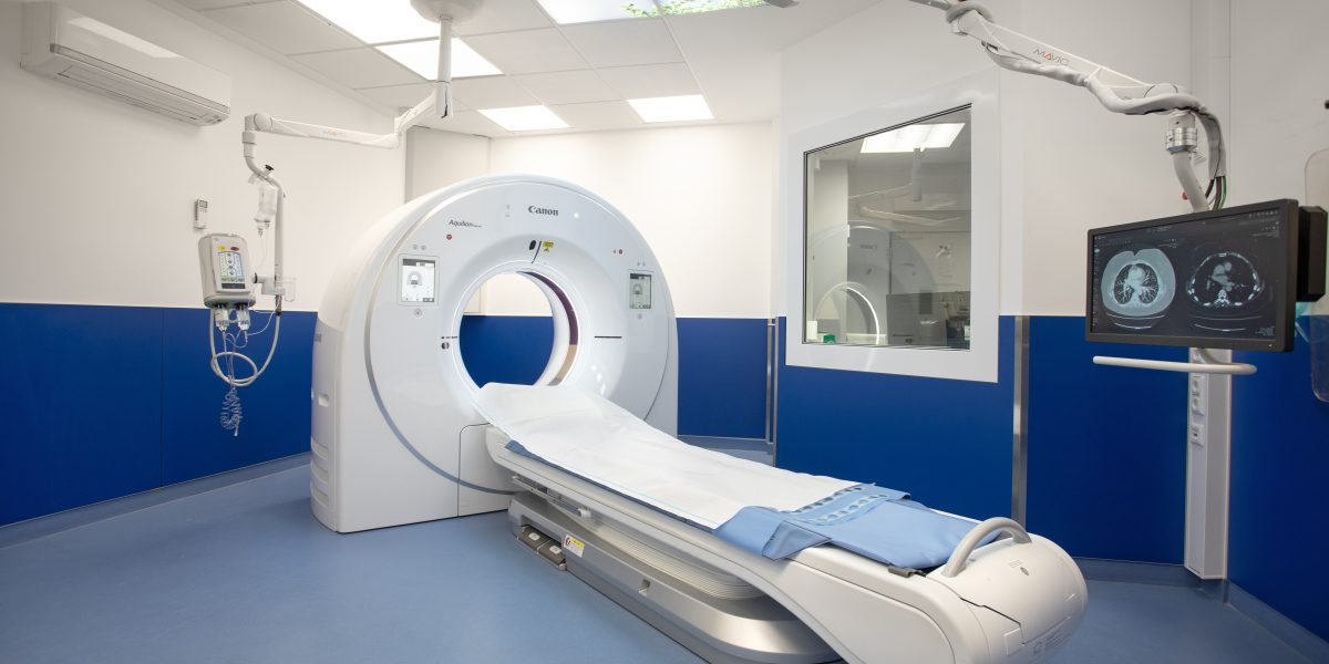 Moderner CT-Scanner in einem Krankenhausräum mit Monitor, blau-weißem Interieur und Bildprojektion an der Decke.