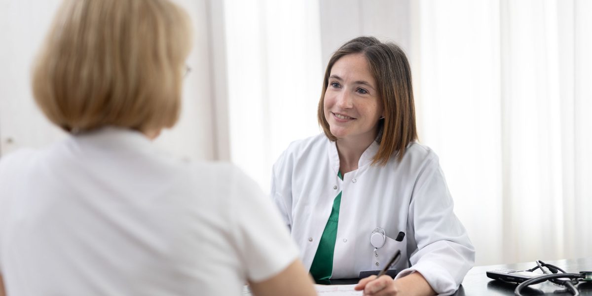 Doctor smilingly talks to a patient at a table, stethoscope next to them.