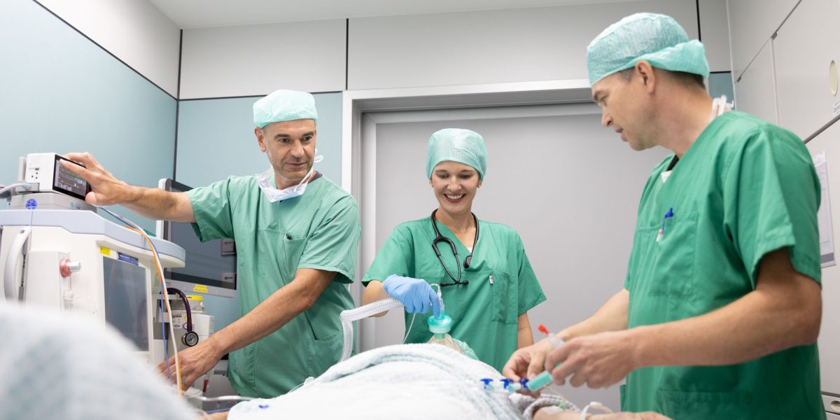 Doctors in green surgical scrubs performing a medical procedure on a patient in a hospital.