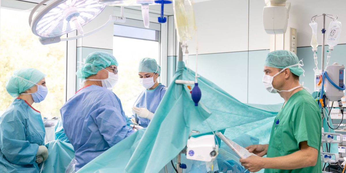 Doctors in the operating room during surgery, surrounded by medical equipment and surgical lights, wearing protective clothing.
