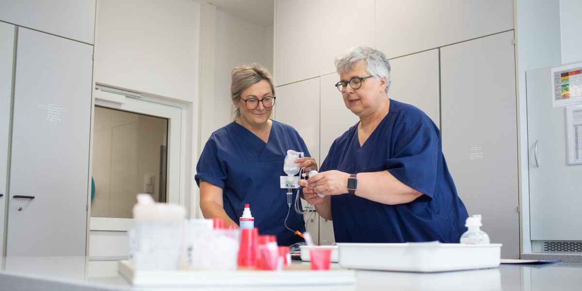 Zwei Pflegekräfte in blauer Dienstkleidung arbeiten gemeinsam in einem Krankenhauslabor.