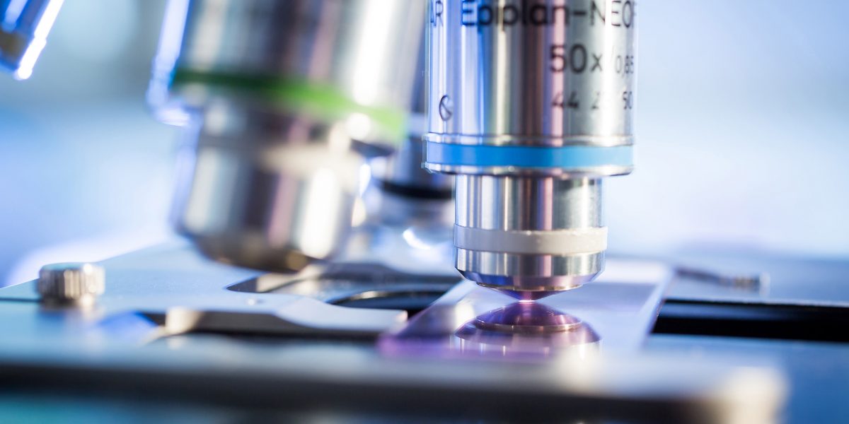 Nahaufnahme eines Mikroskops mit Objektiv, das auf eine Probe fokussiert ist, im Laborlicht.