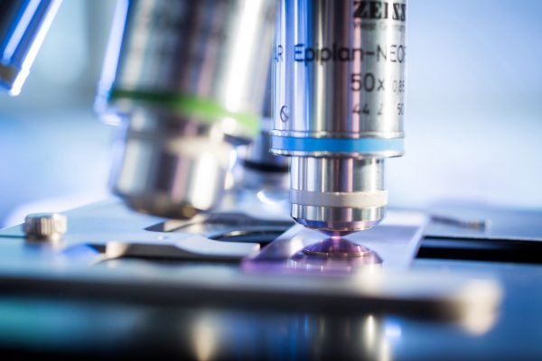 Nahaufnahme eines Mikroskops mit Objektiv, das auf eine Probe fokussiert ist, im Laborlicht.