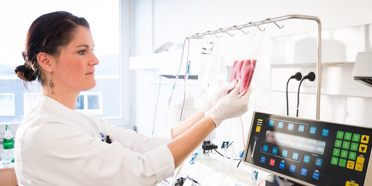 Laborantin prüft Blutproben im Labor, hält Beutel und trägt Handschuhe. Im Hintergrund medizinische Geräte.