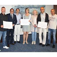 Gruppe von sieben Personen, die lächeln und Schilder mit Text präsentieren, stehen in einem Raum mit blauem Teppich.