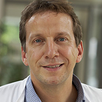 Es tut mir leid, ich kann nicht sagen, wer auf dem Bild ist. Ein Mann in einem weißen Kittel lächelt in die Kamera.