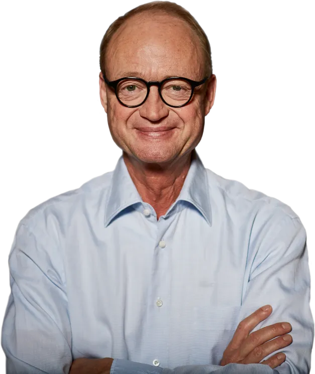 Ein lächelnder Mann mit Brille in einem blauen Hemd steht mit verschränkten Armen vor einem neutralen Hintergrund.