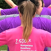 Rückenansicht mehrerer Personen in pinken und lila T-Shirts mit Aufdruck 