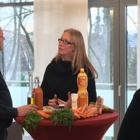 Fernsehteam filmt Interview mit zwei Personen an Tisch, dekoriert mit Karotten und Saftflasche.
