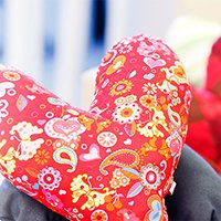 Rotes Herz-Kissen mit buntem Blumenmuster auf unscharfem Hintergrund.