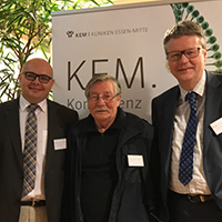 Drei Männer stehen vor einem Banner mit der Aufschrift 