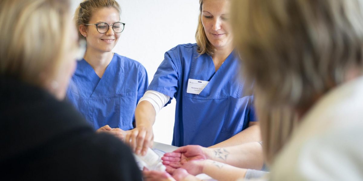 Krankenschwestern in blauen Kitteln unterrichten Menschen im Händewaschen.