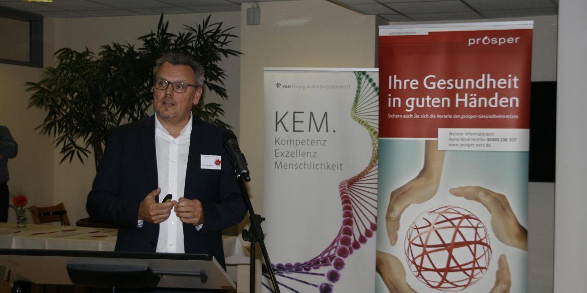 Ein Mann hält eine Präsentation vor zwei Bannern mit den Aufschriften 