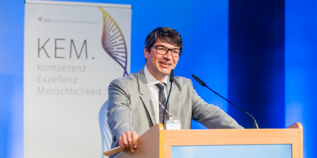 Mann in Anzug spricht am Rednerpult, im Hintergrund Banner mit Aufschrift 