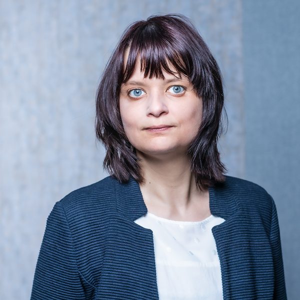 Frau mit schulterlangem, dunklem Haar und blauem Blazer vor neutralem Hintergrund.