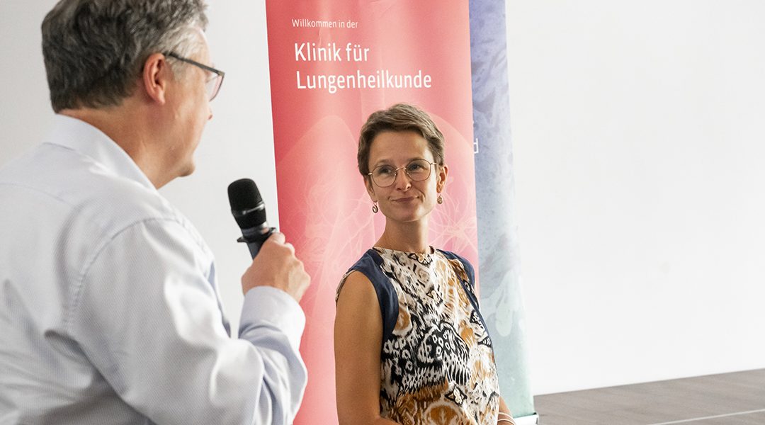 Ein Mann mit Mikrofon spricht zu einer Frau vor einem Banner der Klinik für Lungenheilkunde.