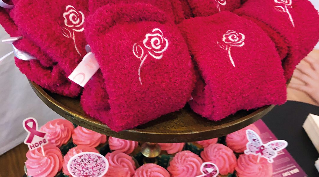 Rosa Handtücher mit Rosenmuster auf einem Ständer, darunter rosa Cupcakes mit dekorativen Schildchen.