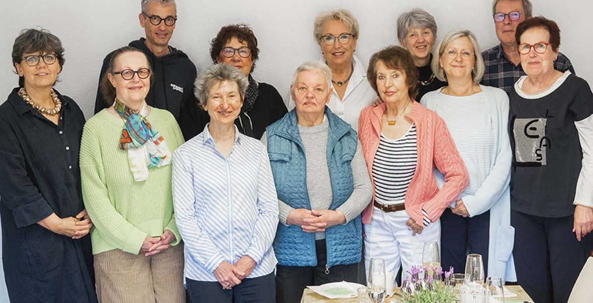Gruppe lächelnder Menschen steht hinter einem gedeckten Tisch mit verschiedenen Gläsern und Geschirr.