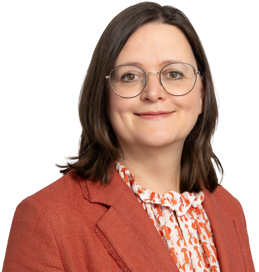 Woman with shoulder-length hair, glasses, and blazer smiles against a light background.