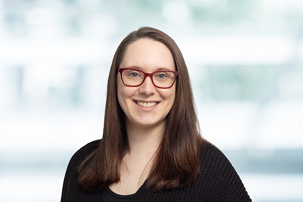 Frau mit langen braunen Haaren und roter Brille lächelt in die Kamera. Sie trägt einen schwarzen Pullover.