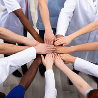 Mehrere Menschen legen die Hände in der Mitte übereinander, symbolisieren Teamarbeit und Zusammenarbeit im Gesundheitswesen.