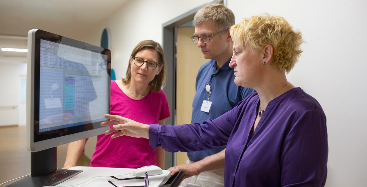 Drei Personen betrachten einen Computermonitor in einem Büro, während eine von ihnen darauf zeigt.