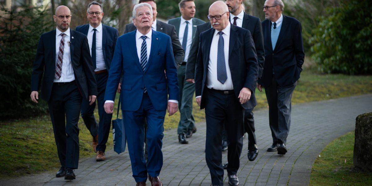 Gruppe von Männern in Anzügen geht auf einem gepflasterten Weg durch einen Park.