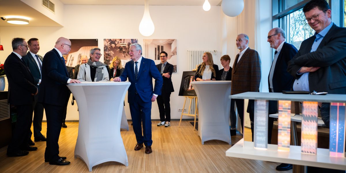 Gruppe von Menschen in Anzügen plaudert in einem modernen Raum an Stehtischen.