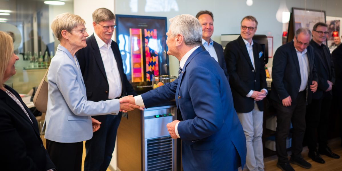 Eine Gruppe von Menschen in Anzügen begrüßt sich per Handschlag in einem modernen Büro.