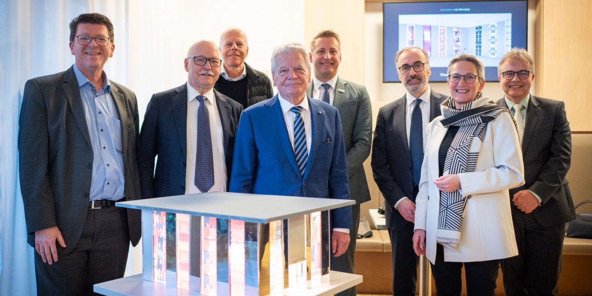 Personengruppe in Businesskleidung posiert lächelnd vor einem beleuchteten Architekturmodell in einem modernen Raum.