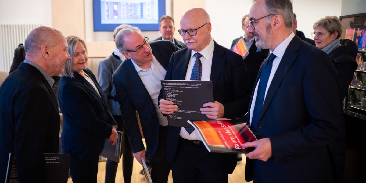 Eine Gruppe von Leuten in formeller Kleidung diskutiert und hält Bücher in einem Innenraum.