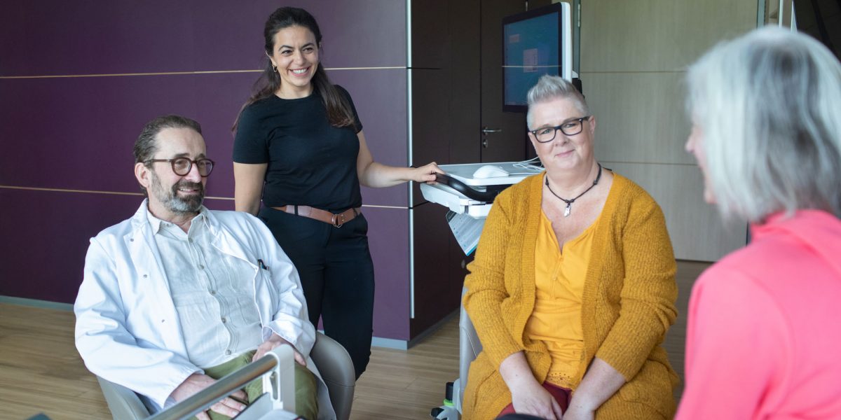 Vier Menschen in einem Krankenhaussitzungsraum, lächelnd und in Gespräch vertieft.