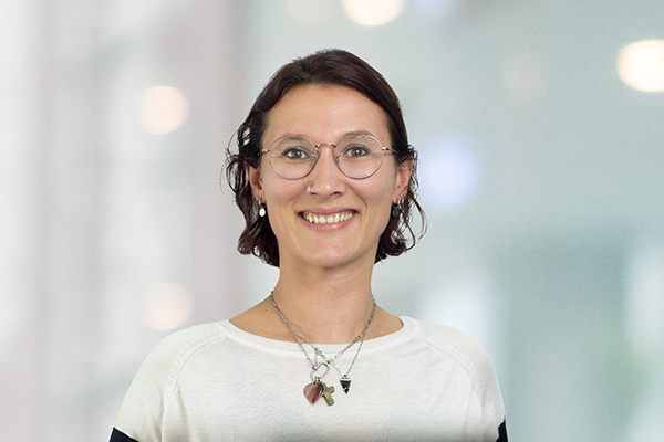 Porträt einer lächelnden Person mit Brille und kurzen Haaren, vor einem unscharfen Hintergrund.